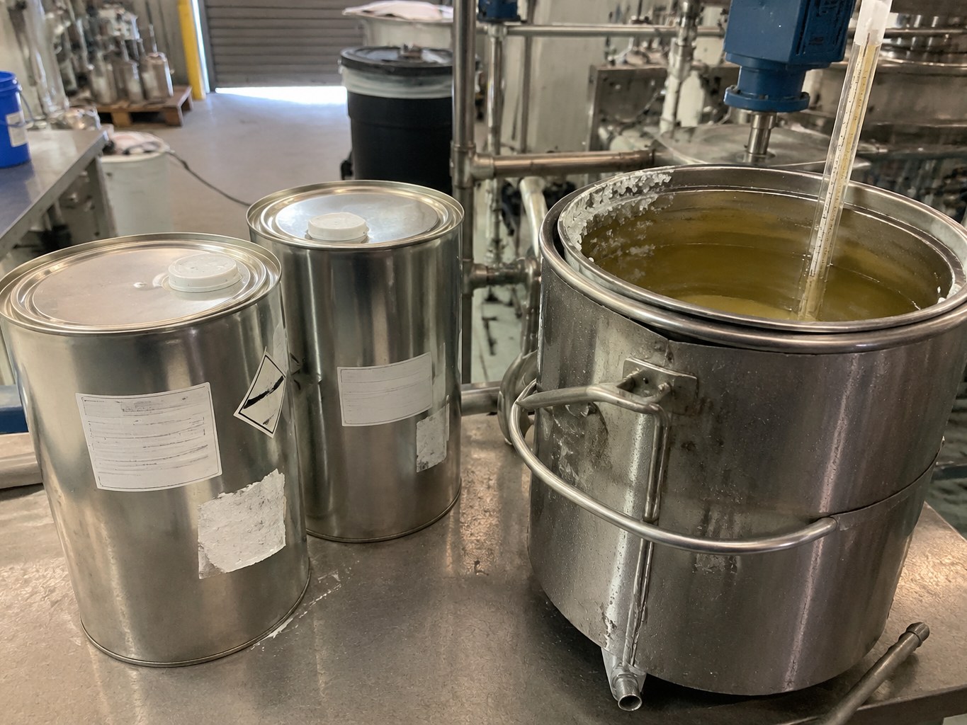 Metal pails of warmed 1-undecanol beside a stainless formulation vessel