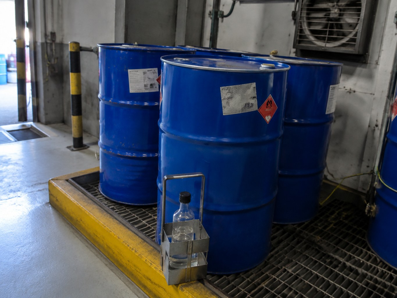 Blue solvent drums and a clear 2-methylpentane sample in a ventilated bund.