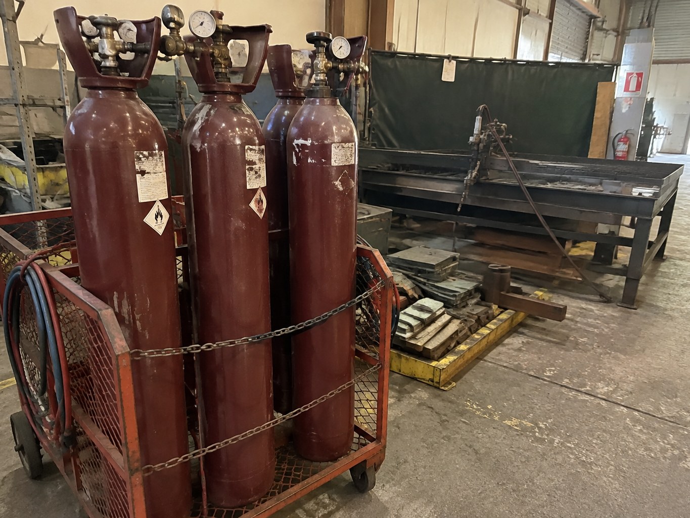 Maroon acetylene cylinders secured on a wheeled cage in a maintained metalworking workshop.