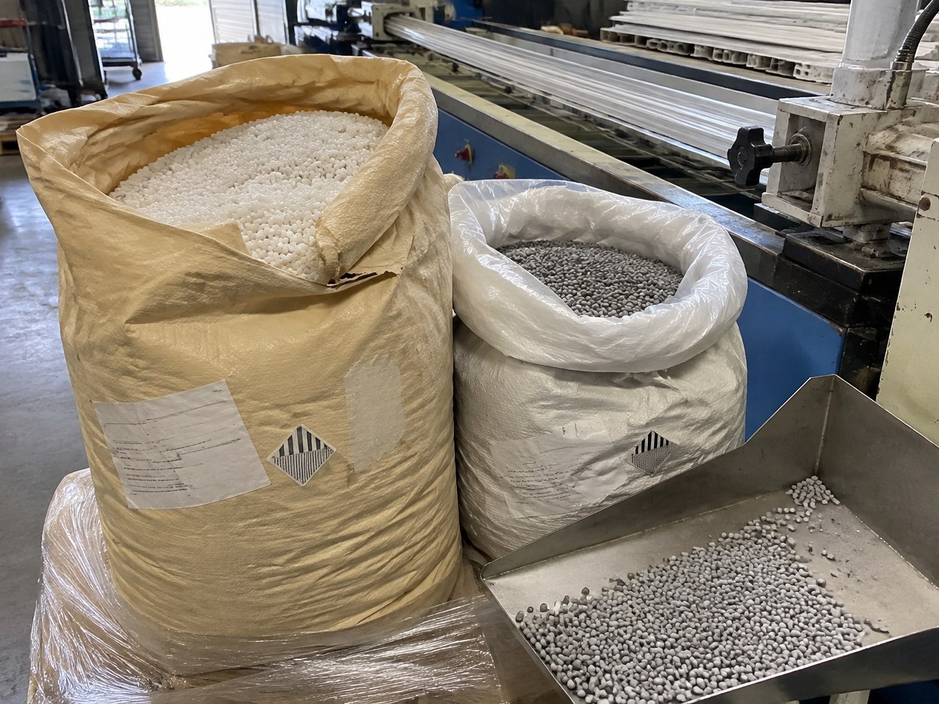 Open sacks of natural and grey ASA resin pellets beside an extrusion line