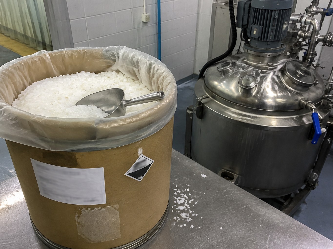 White behentrimonium methosulfate flakes in a lined fibre drum beside a mixer.