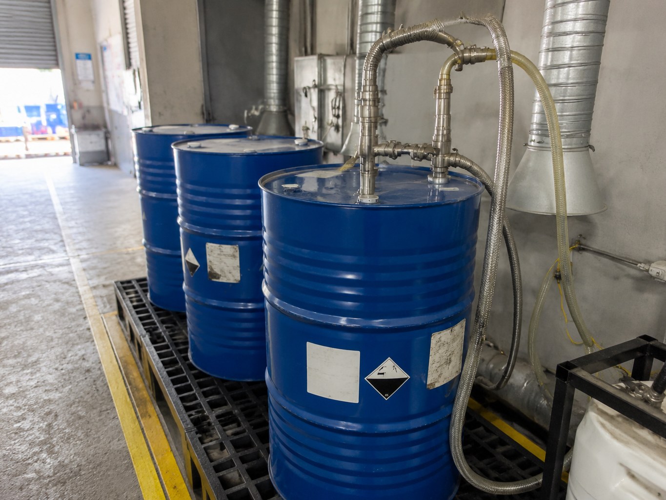 Sealed blue butylamine drums connected to closed transfer hoses in a ventilated bay