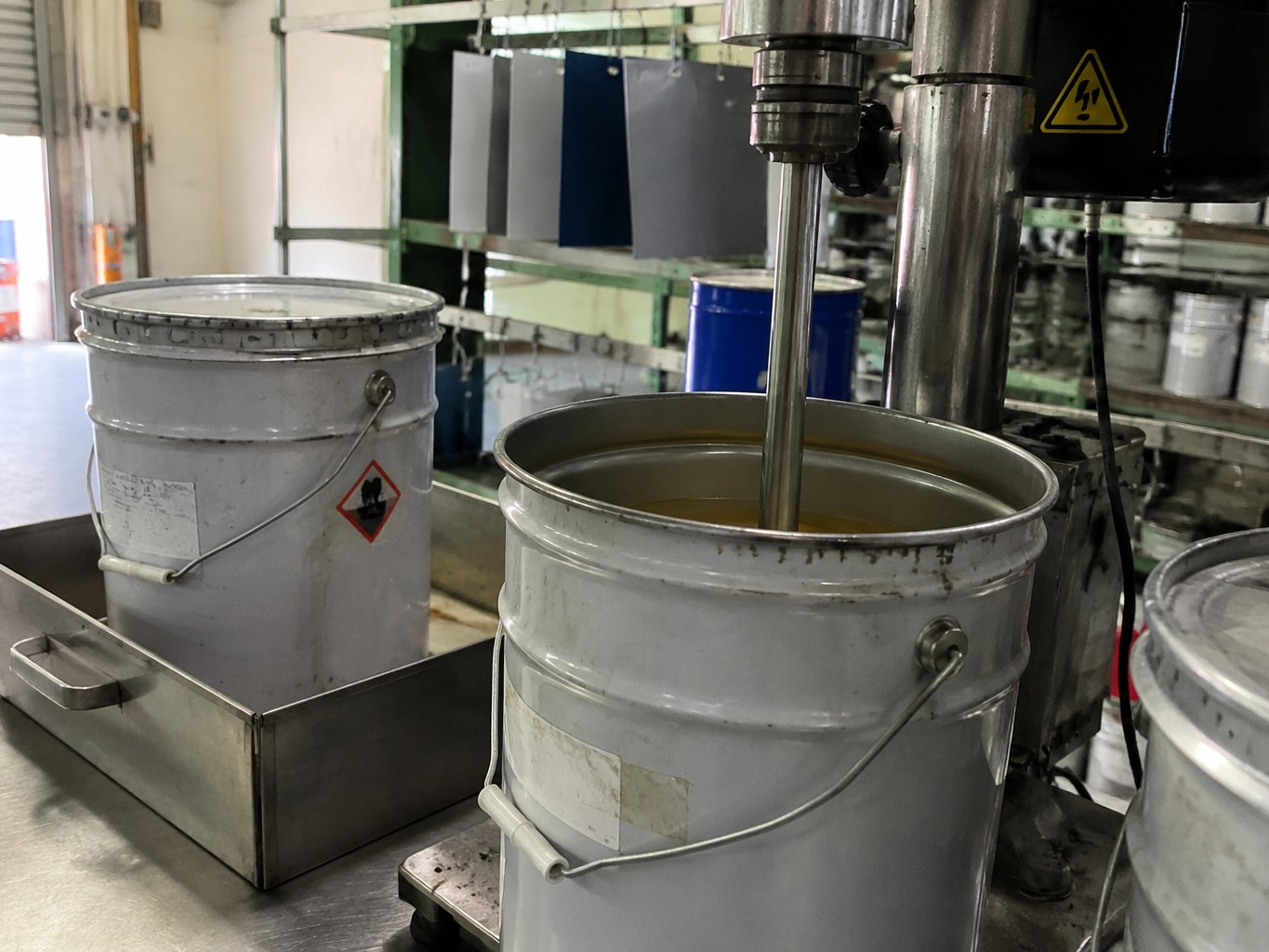 Open metal pails of chlorinated polyolefin solution beside a coating mixer