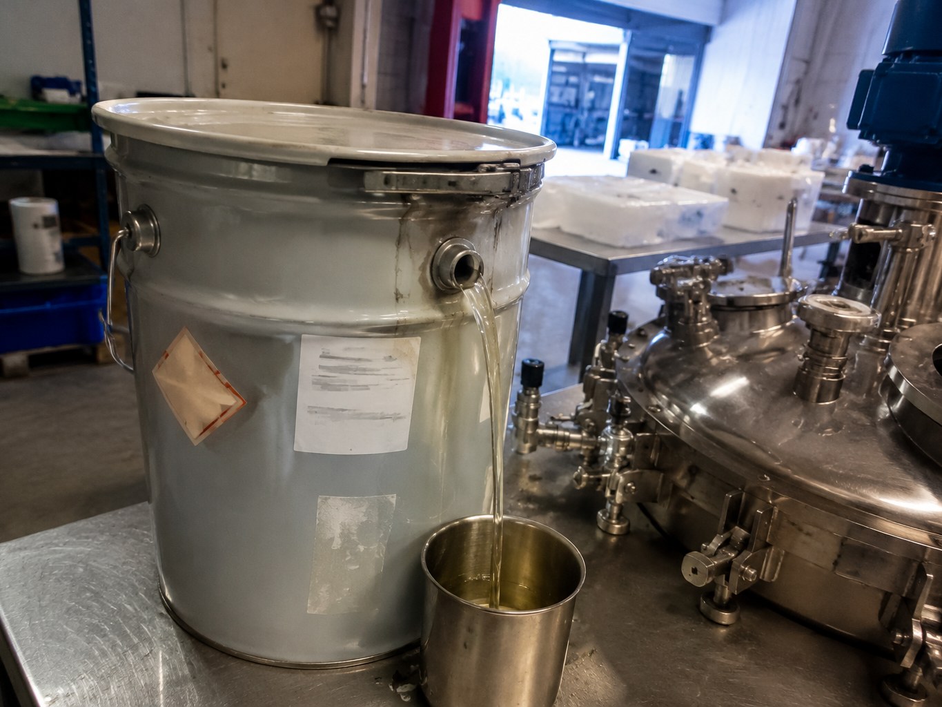 Metal pail of pale cycloaliphatic epoxy resin beside an encapsulation mixing vessel