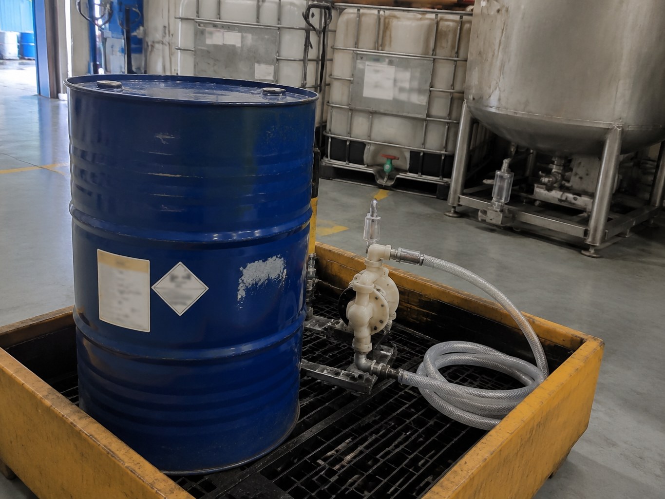 Blue dibutylethanolamine drum with transfer pump inside an industrial containment tray.