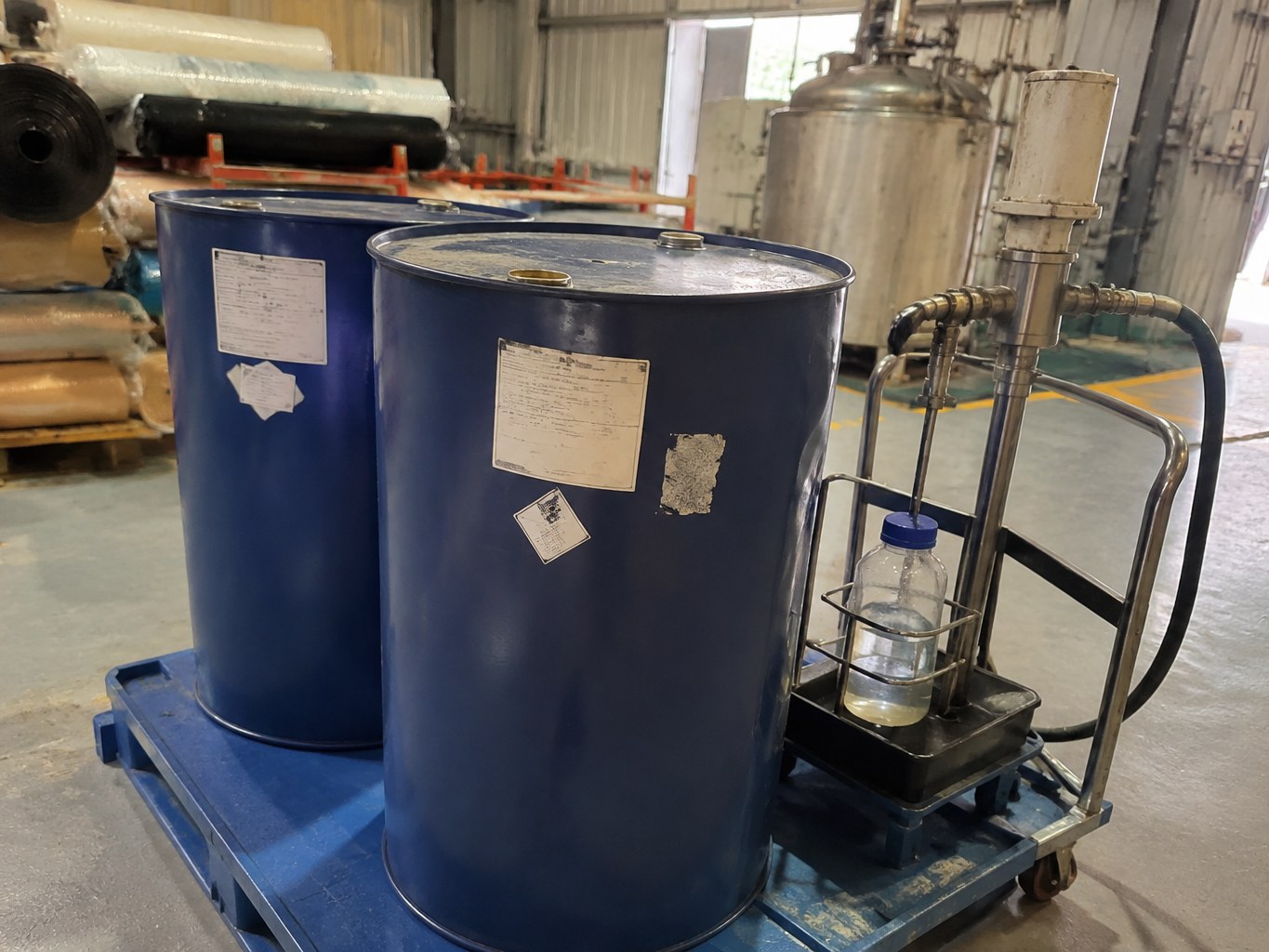 Steel drums of diisobutyl adipate beside a mobile transfer pump in a blending plant.