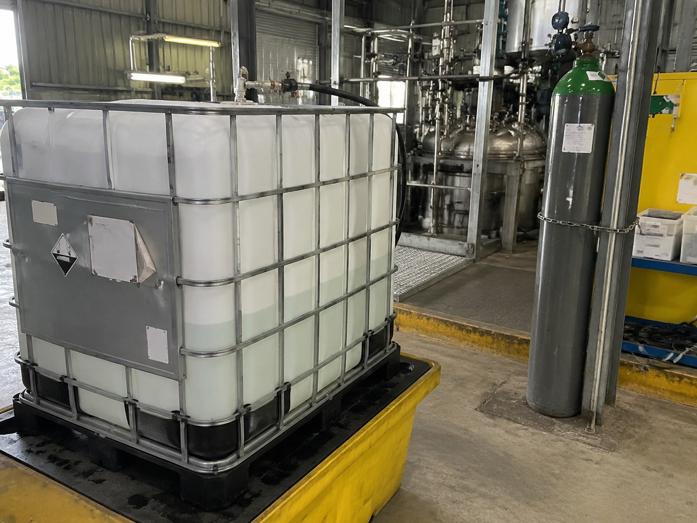 Ethylamine solution IBC with secured gas cylinders in an industrial synthesis area.
