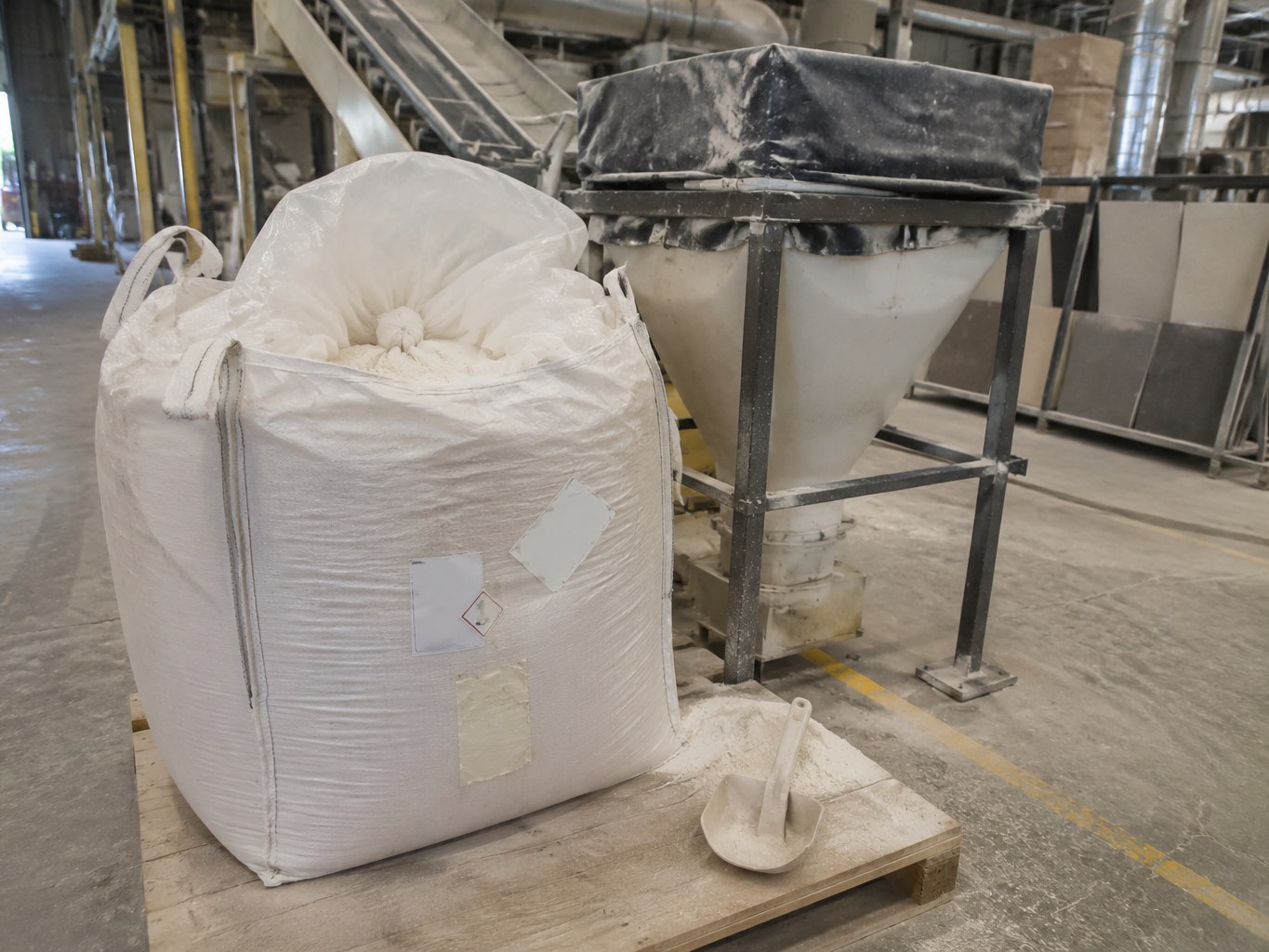 Bulk bag of pale feldspar powder beside a ceramic plant hopper.