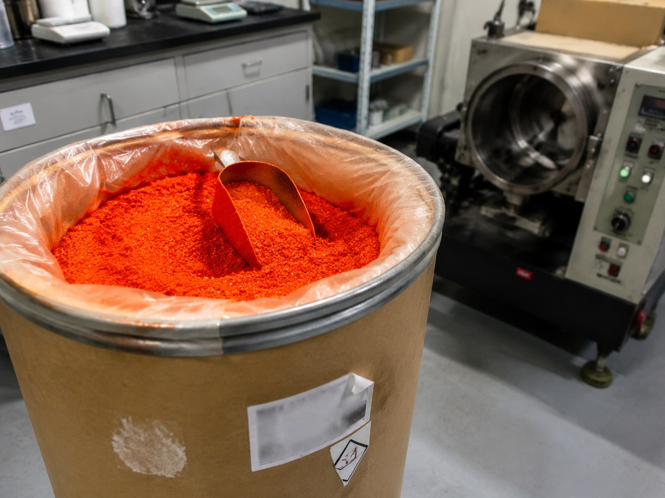 Bright orange ferrocene crystals in a lined fibre drum beside processing equipment.