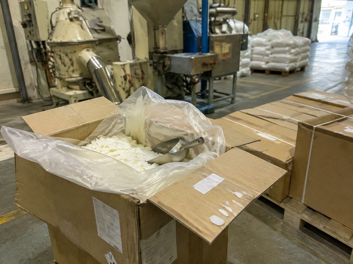 Open lined carton of white glycerol tristearate flakes beside a polymer feeder