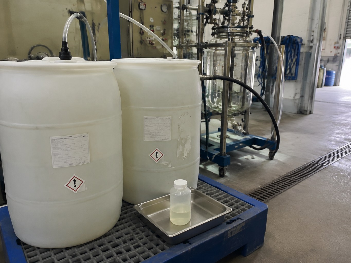 HDPE drums of pale glyoxylic acid solution beside a fine-chemical reactor feed