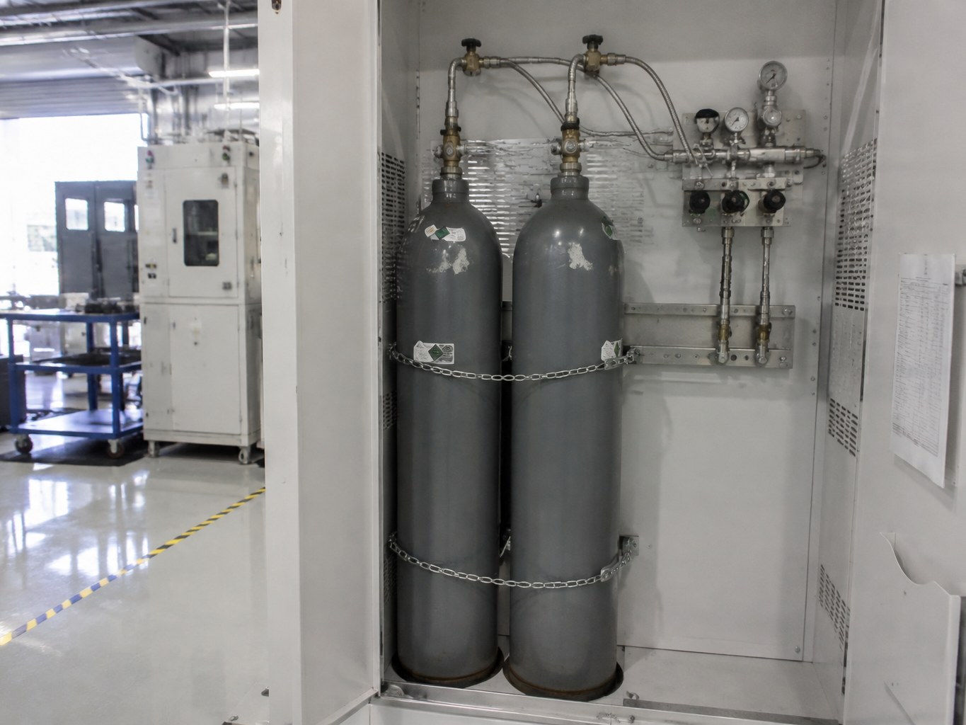 Hydrogen bromide cylinders secured in a ventilated electronics process-gas cabinet.