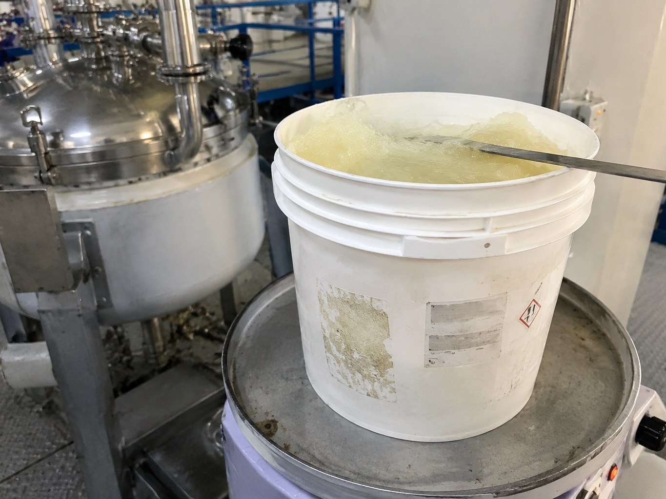 Pale semi-solid isostearic acid in a warmed pail beside a mixing vessel.