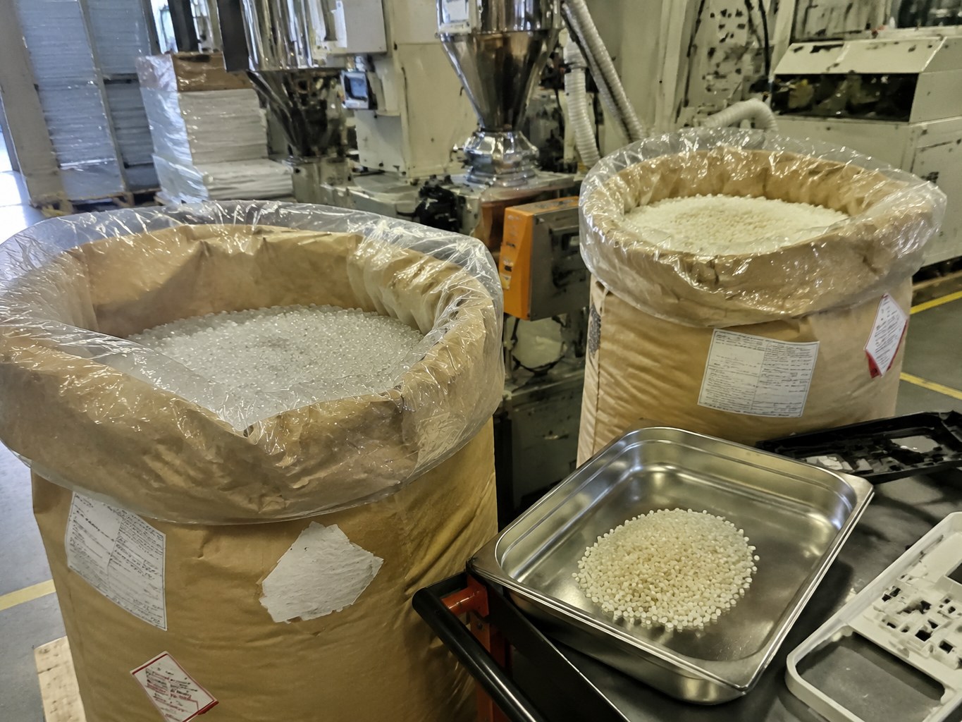 Open sacks of natural MABS resin pellets beside an injection-moulding materials station