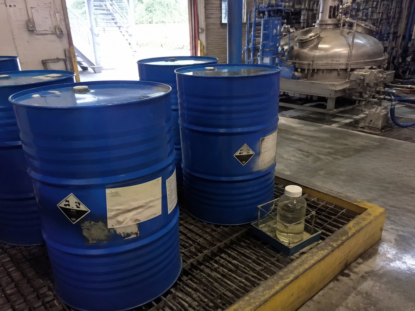Blue octylamine drums and a clear sample inside a ventilated chemical bund.