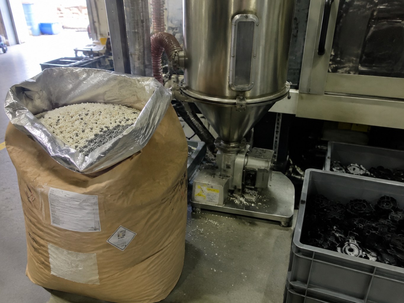 PC/PBT blend pellets in a lined sack beside an injection moulding machine.
