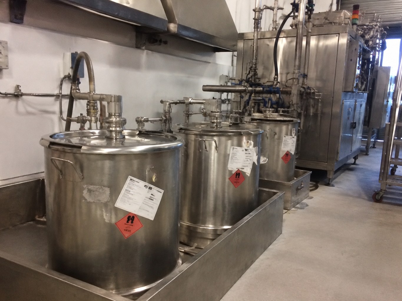 Stainless pentanal containers in a closed transfer bay beside process piping