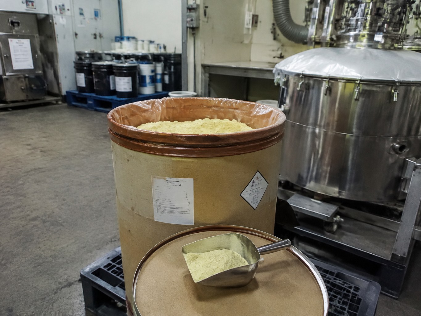 Open drum of pale yellow photoinitiator TPO powder beside a UV-resin mixer.