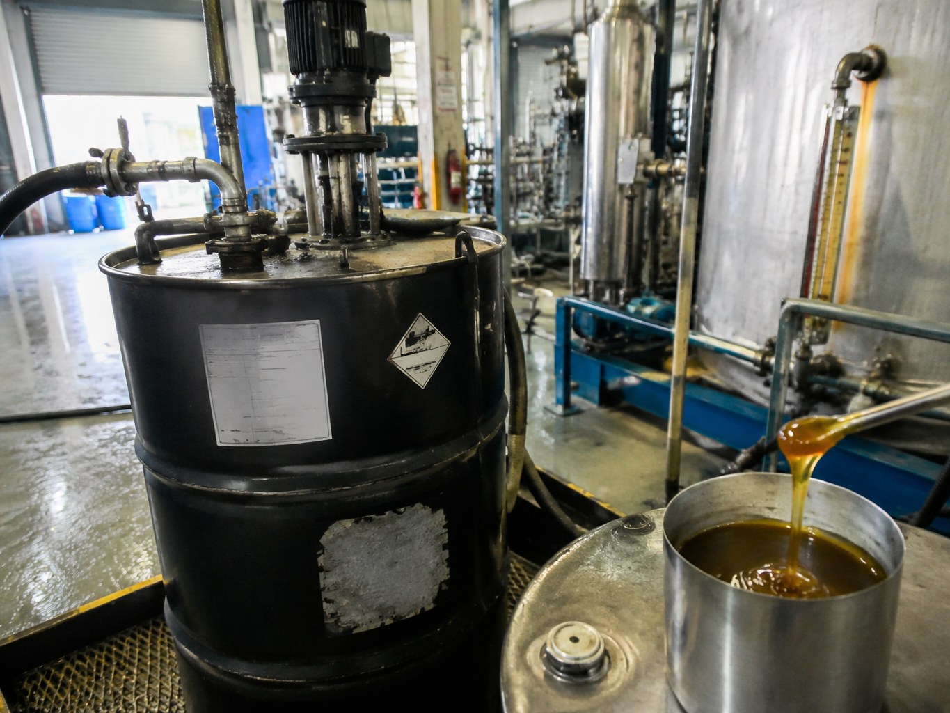 Viscous amber polyisobutylene succinimide draining into a cup beside a mixing vessel.