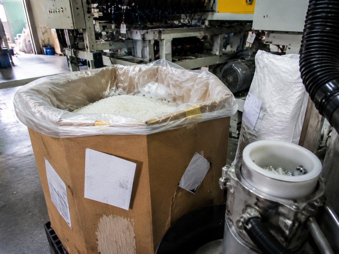 Open bulk box of translucent polyolefin elastomer pellets beside an extrusion line