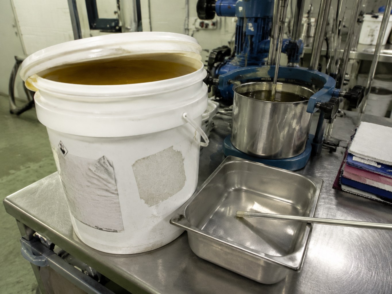 Open pail of amber polyoxyethylene dioleate beside textile-chemical mixing equipment.