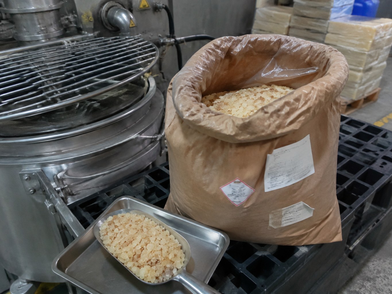Open sack of pale polyterpene resin pellets beside a hot-melt adhesive mixer