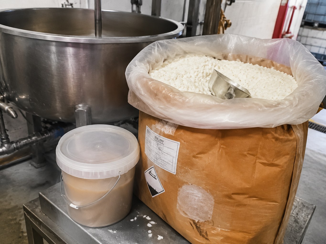 White potassium palmitate flakes in a lined sack beside a soap mixing kettle.