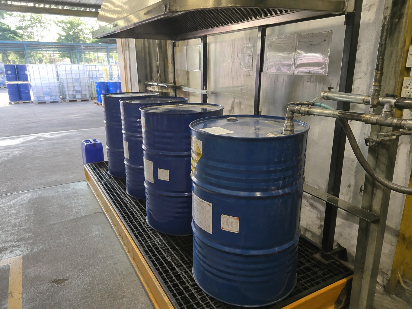 Blue propylamine drums connected to closed transfer hoses in a ventilated bay