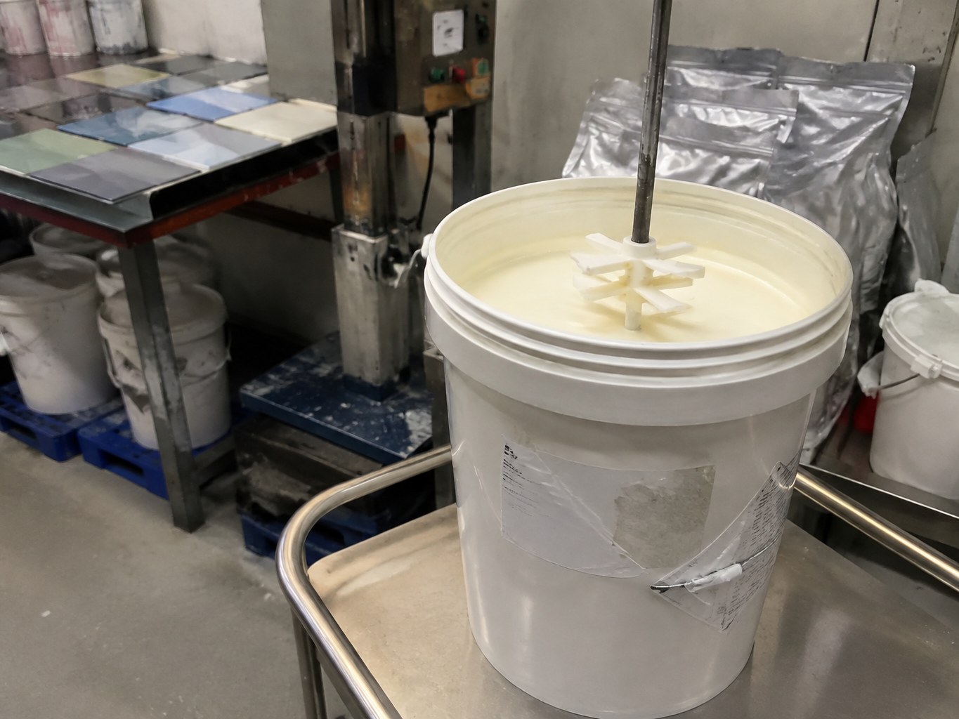 Open pail of creamy pyrithione zinc dispersion beside coating formulation equipment.