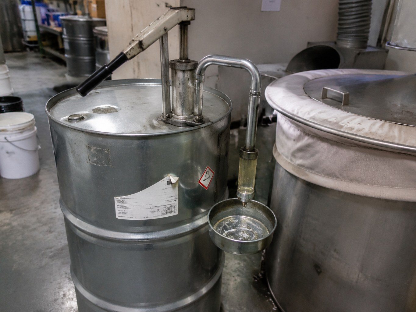 Stainless sec-butanol container beside a covered coatings mixing vessel and transfer pump