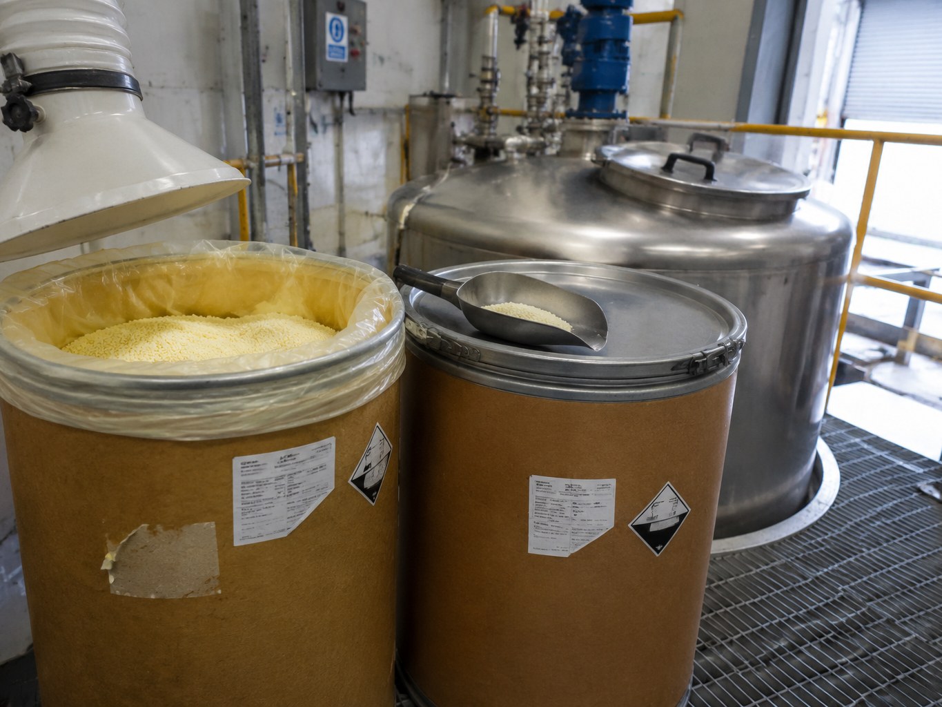 Open fibre drum of pale sodium ethyl xanthate granules beside a clean make-down tank