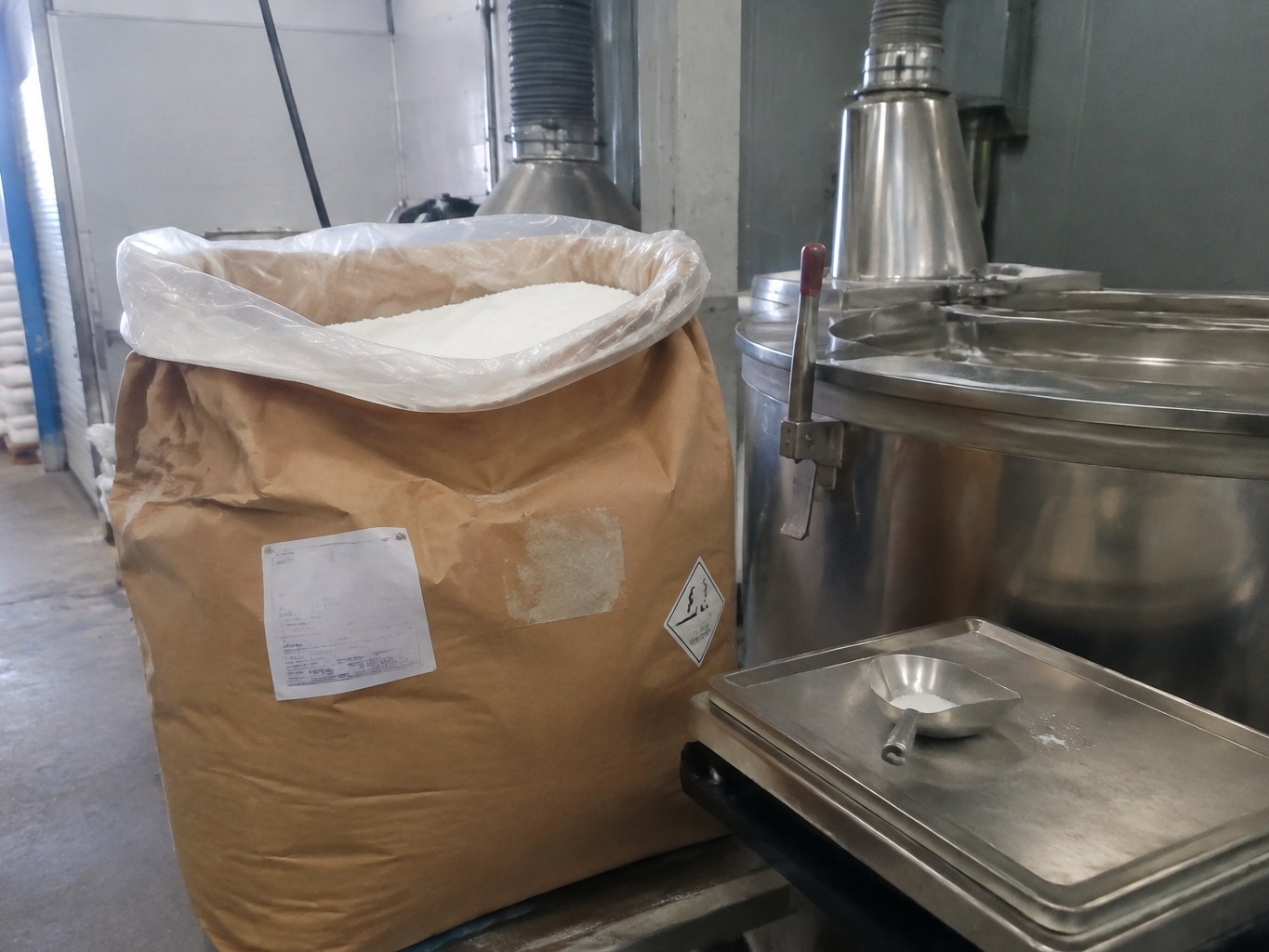 Open sack of white sodium lauryl sulfoacetate granules beside a surfactant mixer.