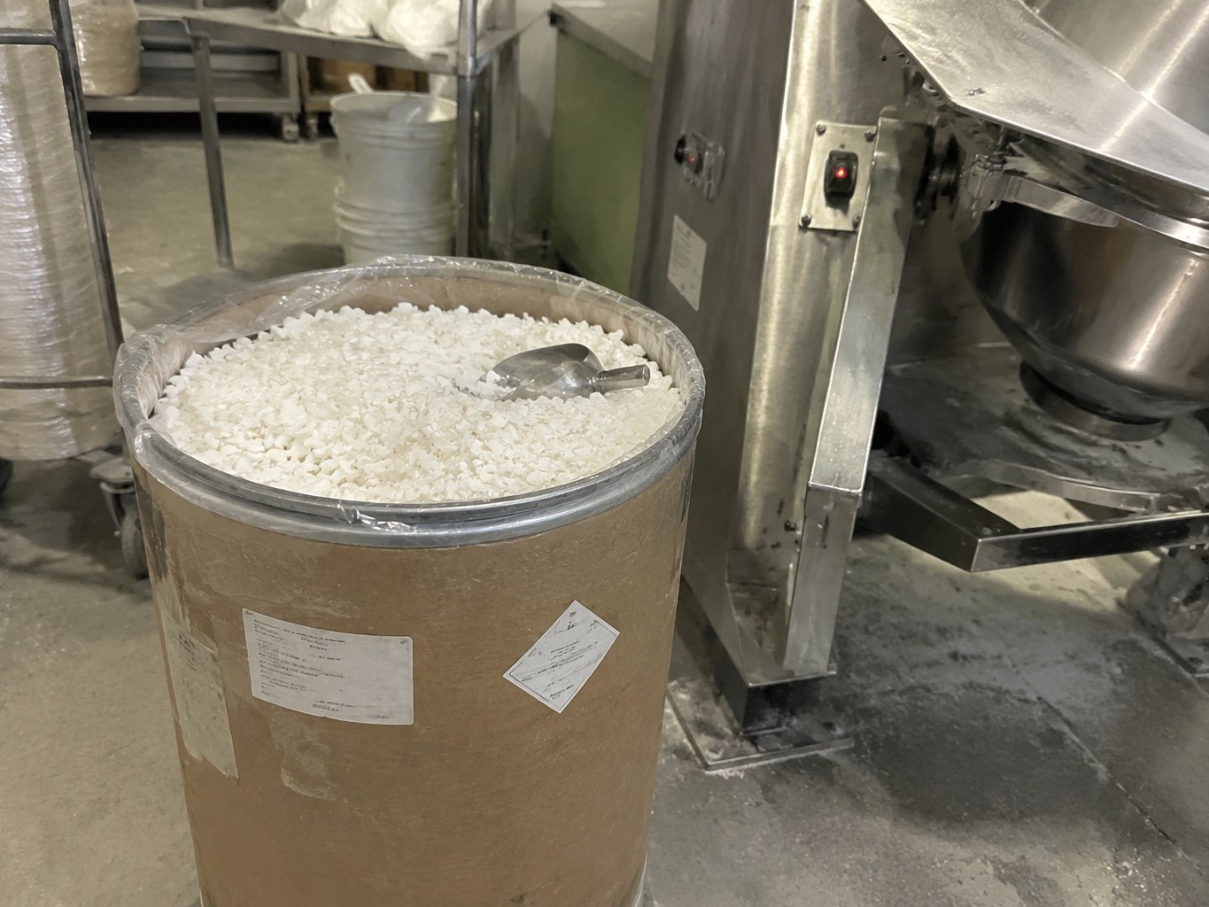 White sodium myristate granules in a lined fibre drum beside a powder mixer.