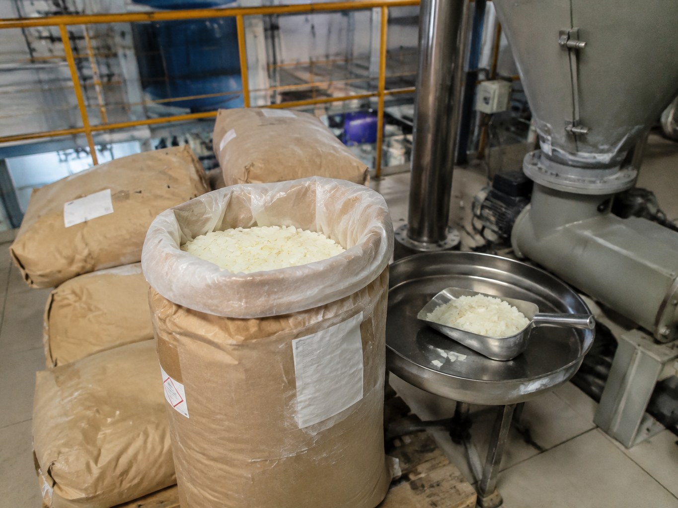 Open sacks of cream sodium palmitate flakes beside a soap production hopper