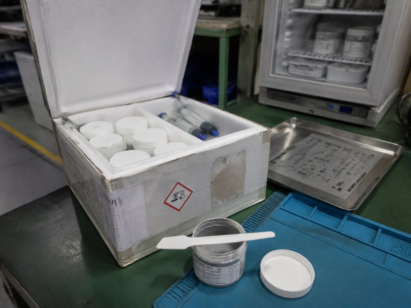Insulated box holding solder paste jars and syringes on an electronics assembly bench