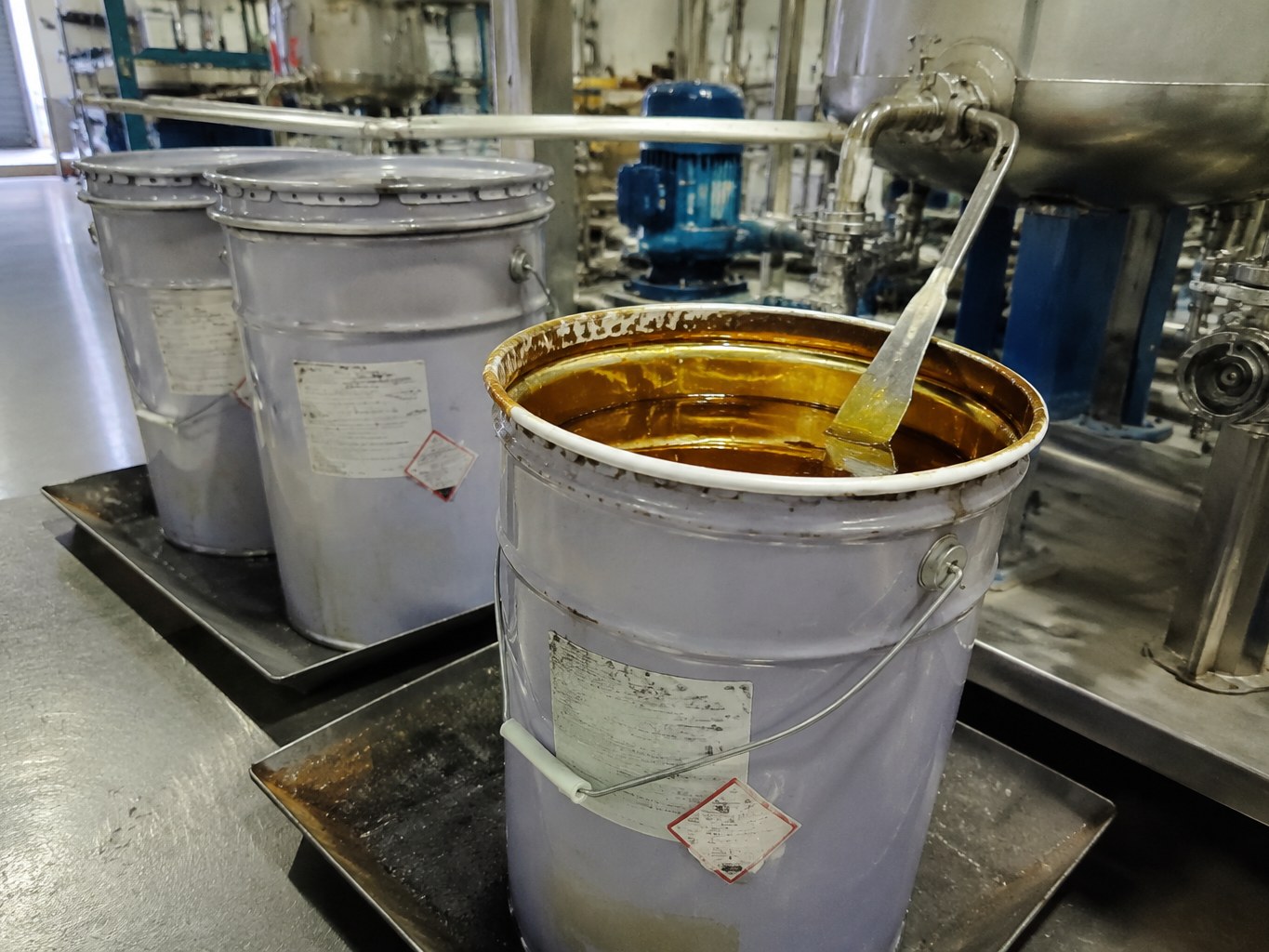 Viscous amber sorbitan trioleate in an open pail beside a blending vessel.