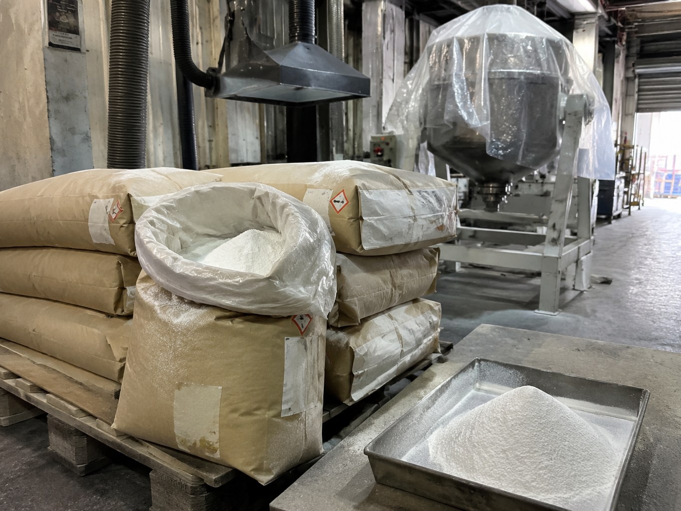 Lined sacks and tray of fine white strontium carbonate beside a ceramics blender