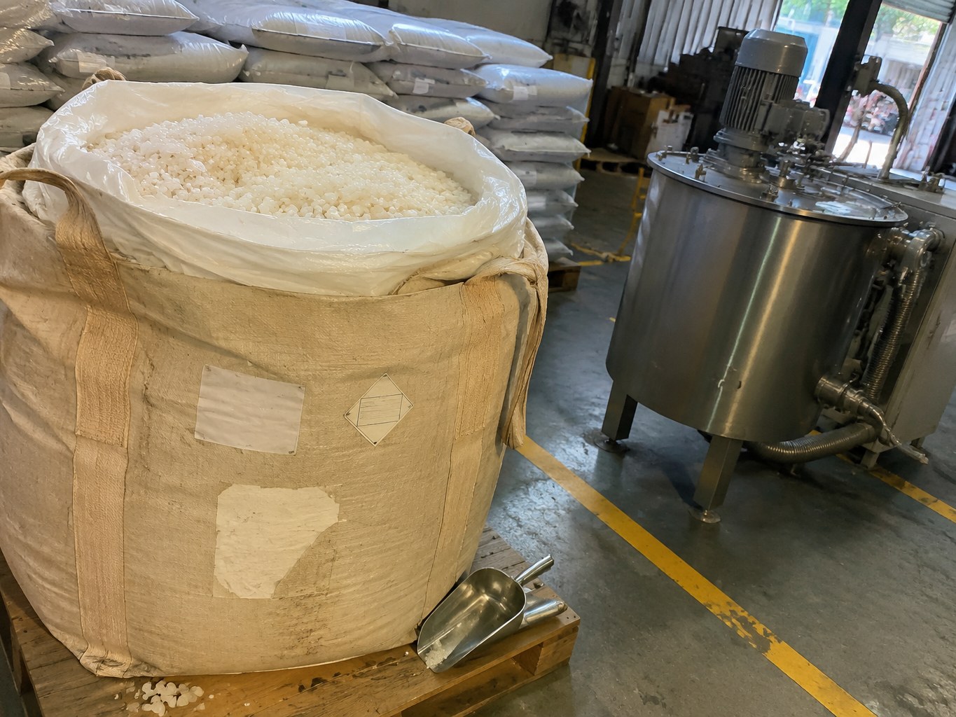 Open bulk sack of pale SBS pellets beside a hot-melt adhesive mixer.