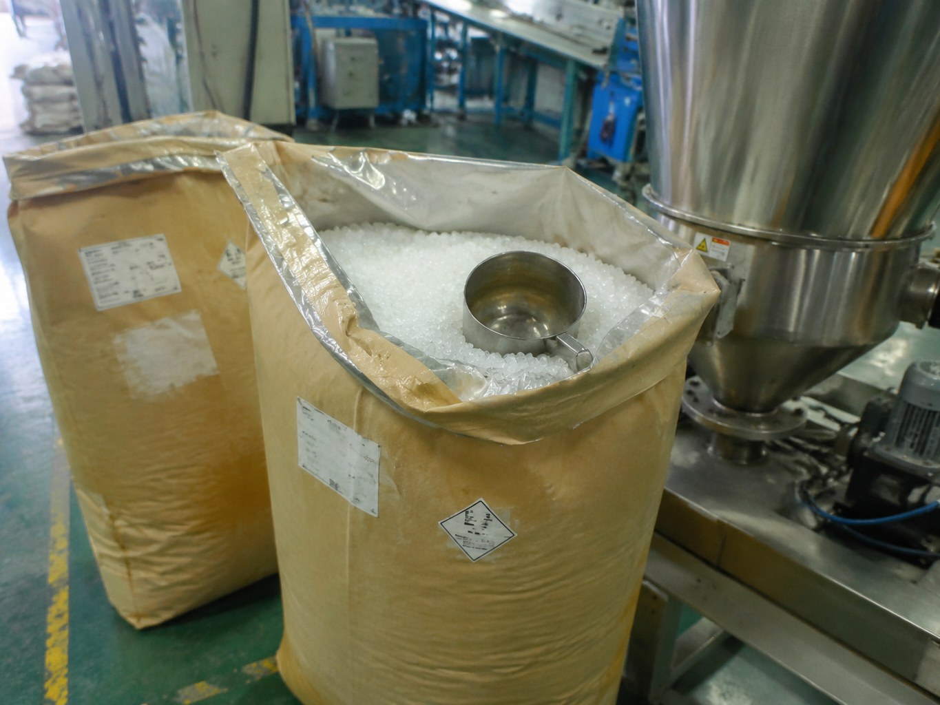 Lined bulk sacks of white SEBS pellets beside a polymer feed hopper.