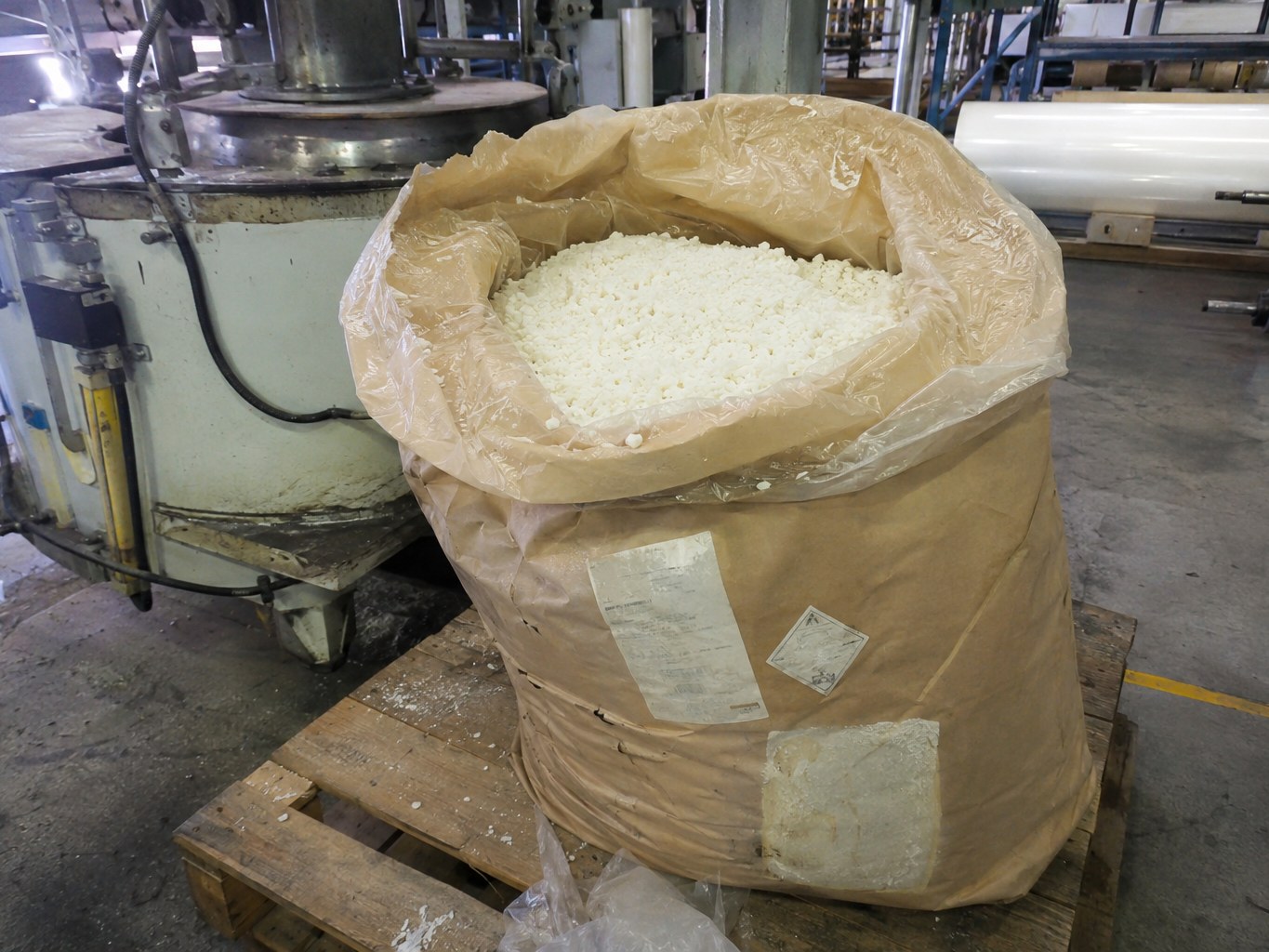 Open sack of pale styrene-isoprene-styrene granules beside an adhesive mixer.