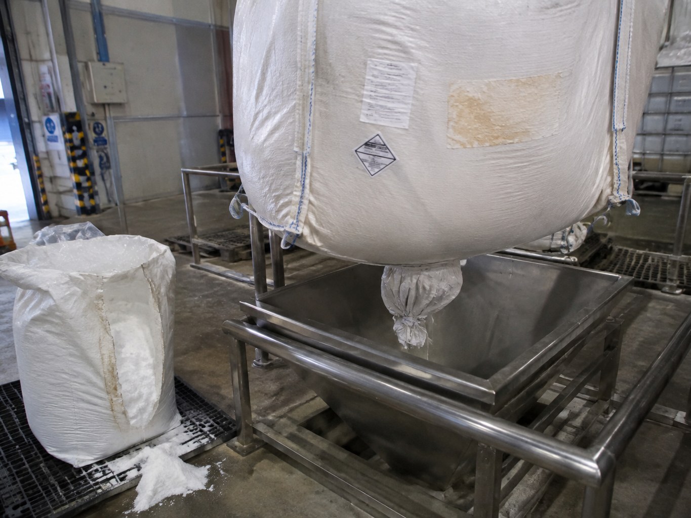Terephthalic acid bulk bag discharging white powder into a stainless hopper.