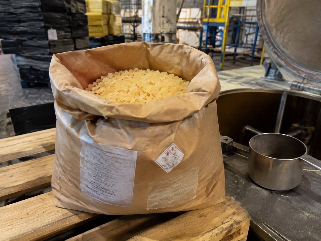Open sack of amber terpene phenolic resin flakes beside an adhesive mixing vessel
