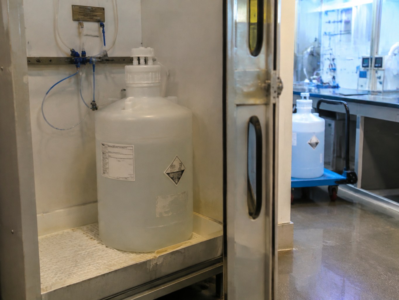 Clear TMAH solution in a sealed carboy inside a semiconductor chemical cabinet.