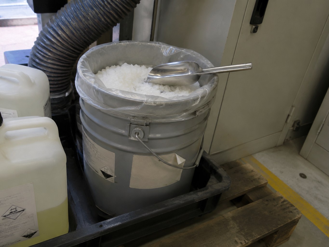Open pail of white tin(IV) chloride crystals beside sealed chemical containers