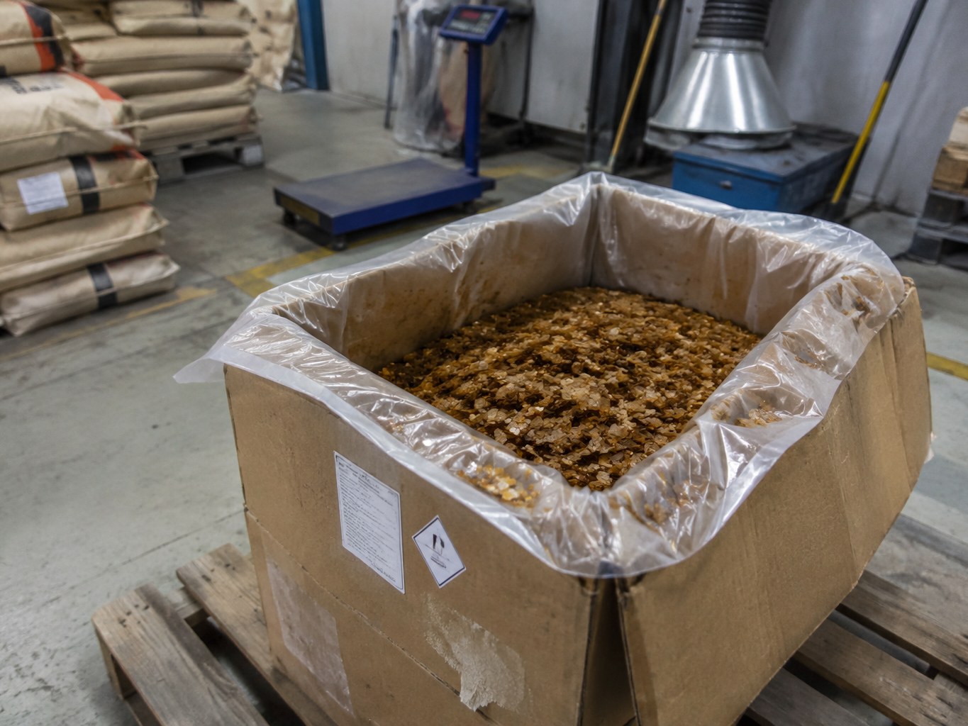 Lined carton filled with brown TMQ antioxidant flakes in a rubber-additive warehouse.