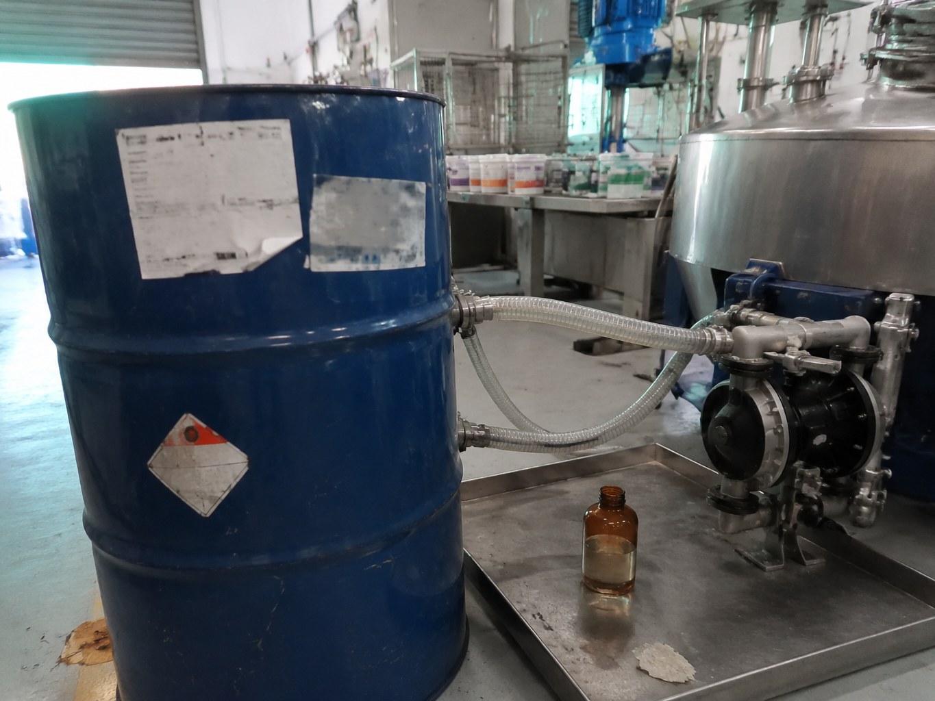 Blue TPGDA drum connected to a UV-coatings mixing vessel in production