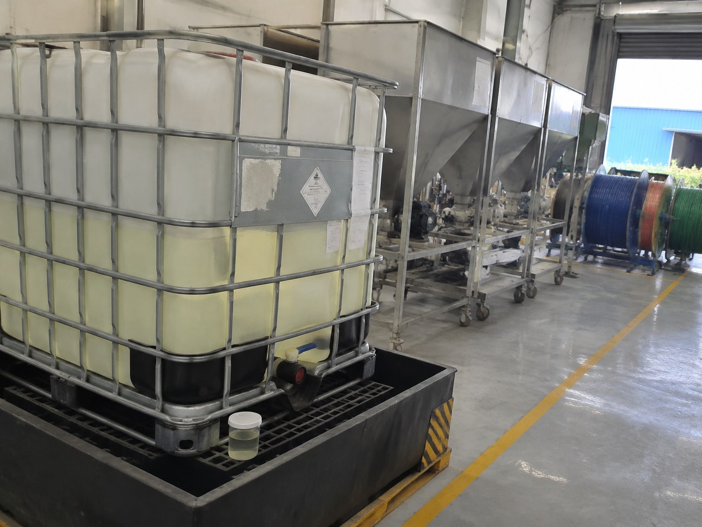 Pale oily TOTM plasticiser in an IBC beside cable compounding equipment.