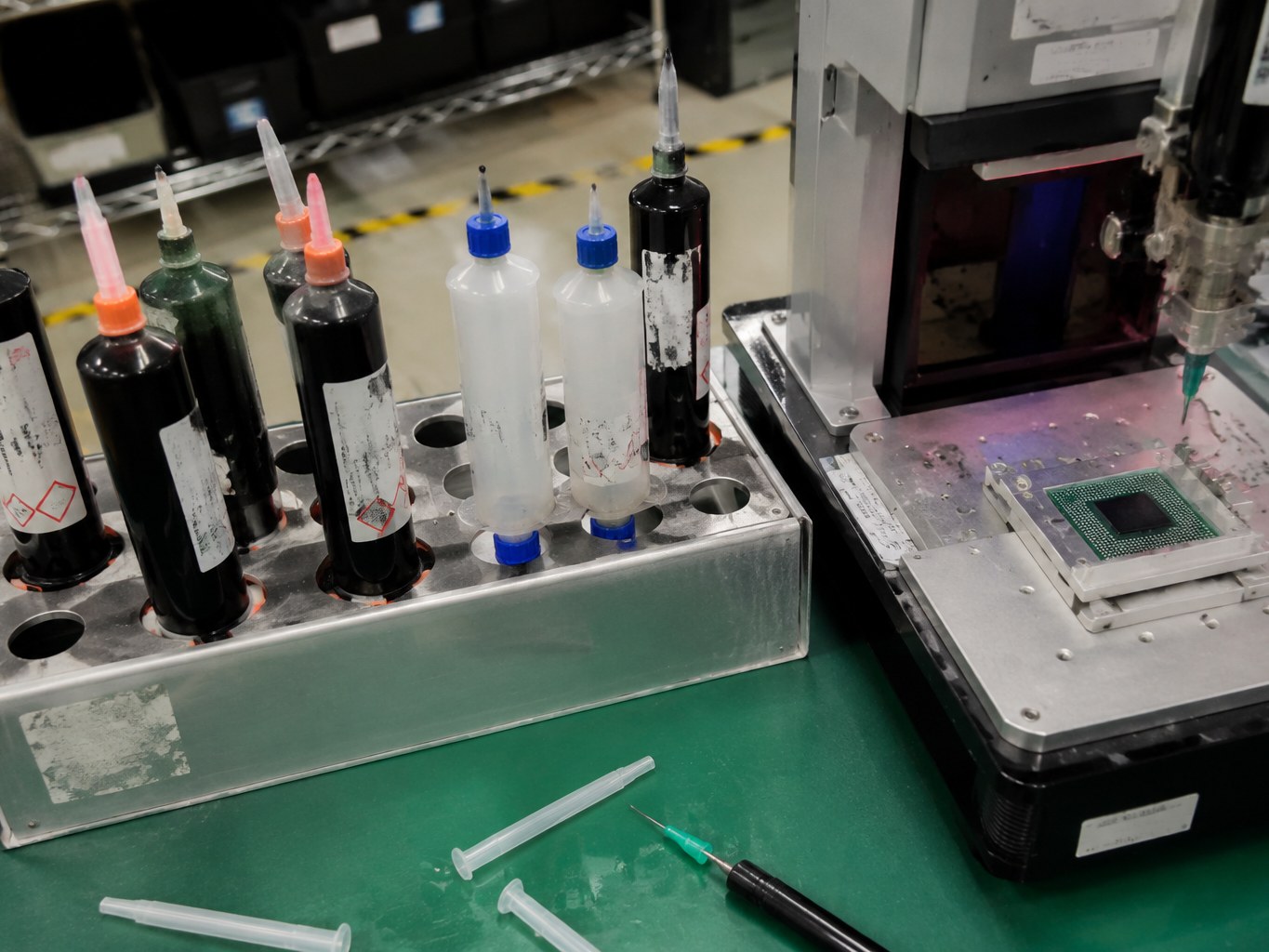 Underfill encapsulant dispensing cartridges beside a semiconductor package assembly fixture.