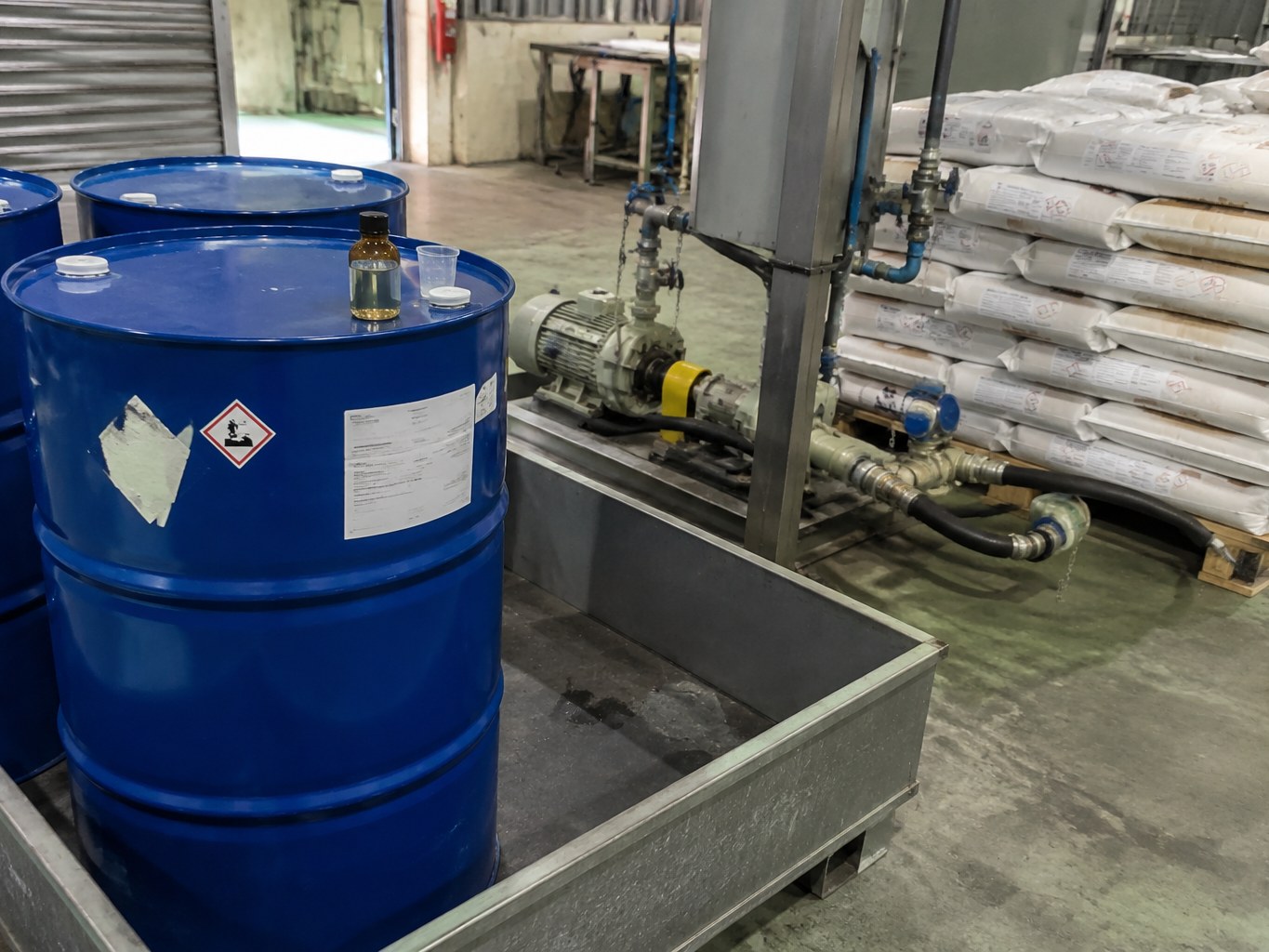Vinyltriethoxysilane drums connected to a transfer line beside stacked raw-material sacks.