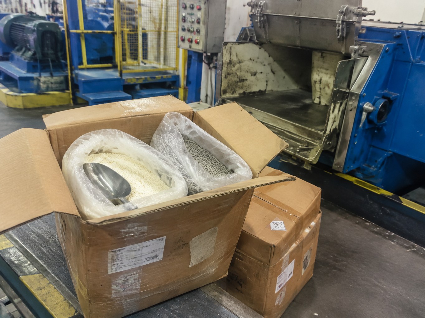 Zinc dimethyldithiocarbamate powder and granules in lined cartons beside rubber compounding equipment.